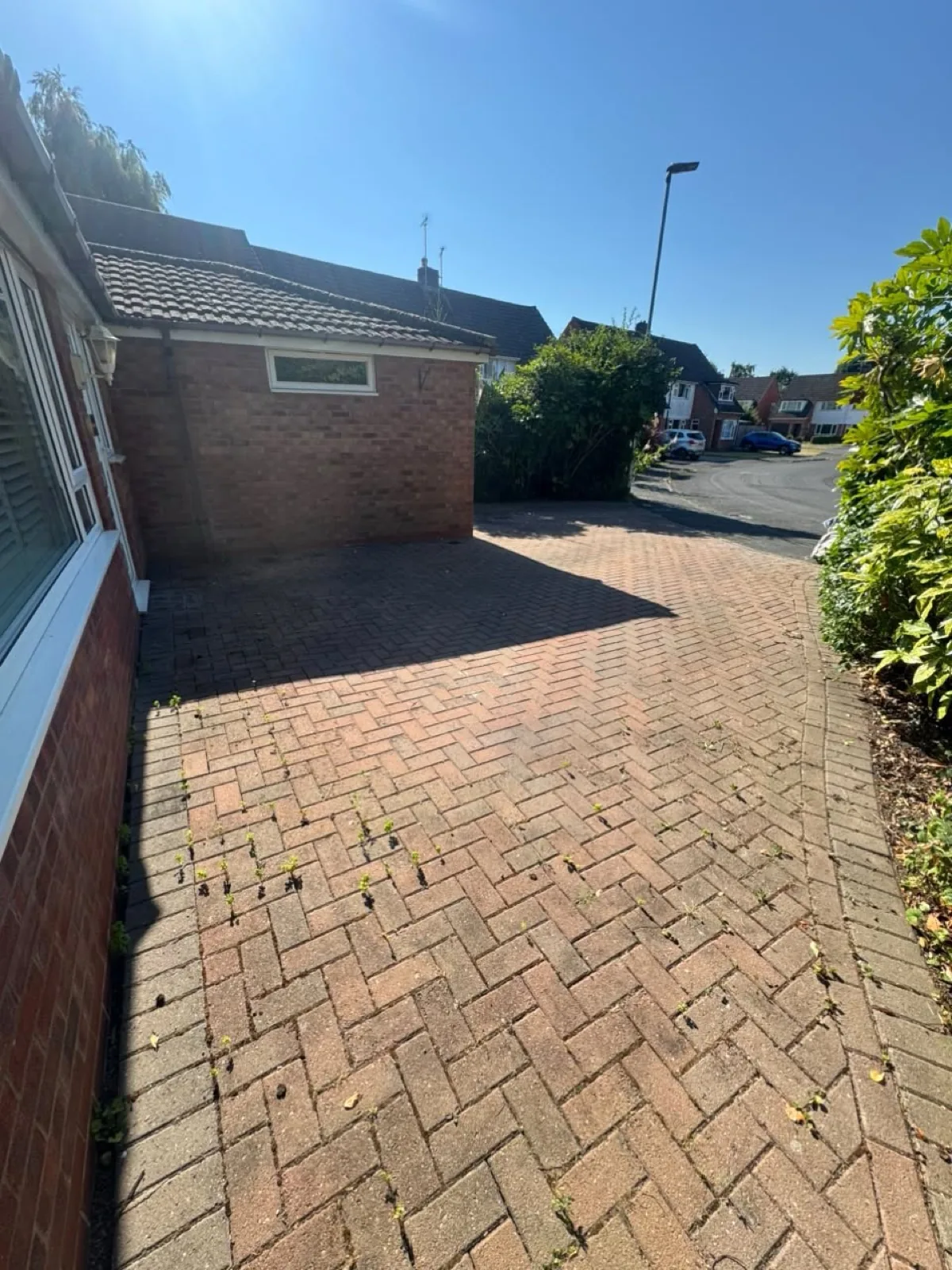 Block-paving driveway before cleaning — faded, with weeds growing in the joints