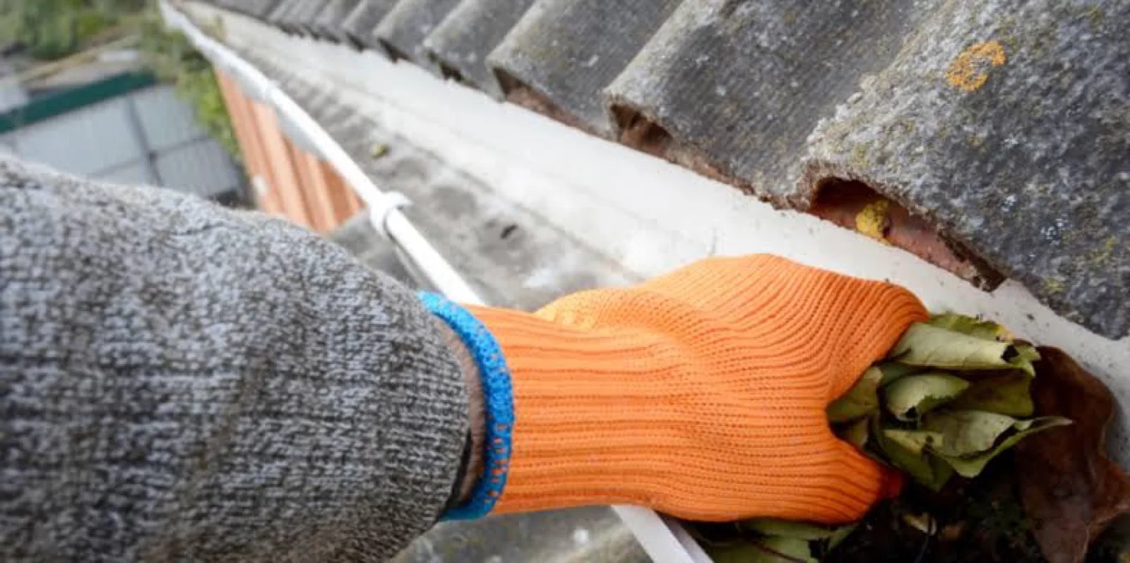 Leaves and debris being cleared from a gutter by hand